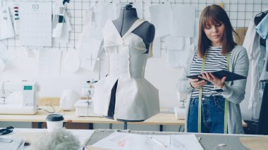 Girişimci tasarlama genç kadın moda giyim mankeni terzilik için pinned denetlerken tablet ile çalışıyor. Modern teknolojileri kavramı üretim kıyafetler.