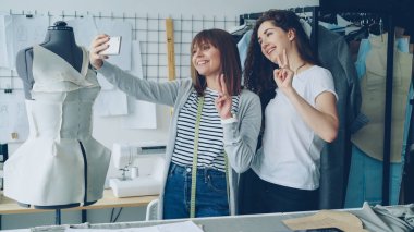İki neşeli kadın giyim tasarımcıları giyinik manken yanında dururken akıllı telefon ile komik selfie studio yapıyoruz. Çekici kadın gülümseyerek ve poz.