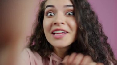 Pembe arka plandaki video görüşmesi sırasında kameraya bakan heyecanlı genç bayanın yakın çekimi. İnsanlar ve iletişim konsepti.