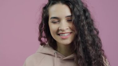 Güzel bir genç bayanın portresi. El hareketi yapıyor ve pembe arkaplanda gülümsüyor. Duygular ve ifadeler kavramı.