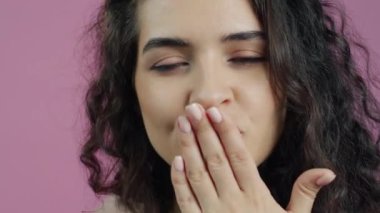 Havadan öpücükler gönderen ve pembe arka planda gülümseyen neşeli kızın yakın plan portresi. Flört ve olumlu duygular kavramı.