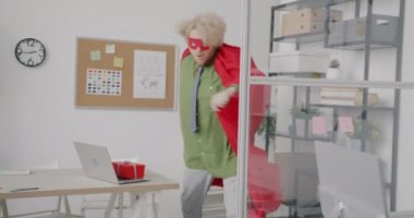 Süper kahraman pelerinli ve maskeli genç adam boş bir ofiste yürüyor ve hediyeler bırakarak işine yardım ediyor. Şirket hayatı ve komik insanlar konsepti..