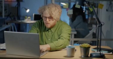 Komik obez iş adamı geceleri karanlık ofiste dizüstü bilgisayarla çalışıp halterle egzersiz yapıyor. Fazla mesai ve spor konsepti.