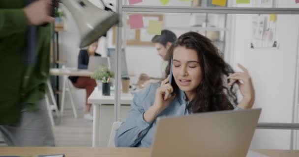 怒り狂った上司がオフィスの部屋でスピーカーで叫んでいるときにケアフリー若い女性が携帯電話でチャットしています 雇用と感情の概念 — ストック動画