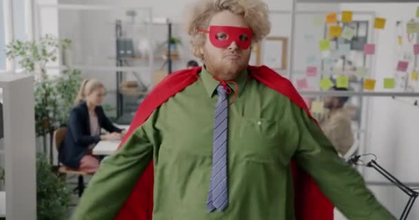穿着超级英雄服装的胖胖的上班族在工作时表现得很有肌肉 而一群人却在幕后工作 — 图库视频影像