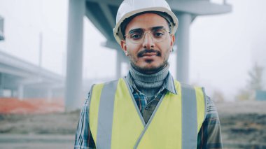 İnşaat alanında üniforma giyen ve kameraya bakan Ortadoğulu müteahhit portresi. Meslek ve uzmanlık kavramı.
