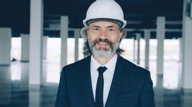 Modern boş bir binada güvenlik kaskı ve resmi takım elbise giymiş başarılı bir emlak yatırımcısının portresi. Halk ve meslek kavramı.