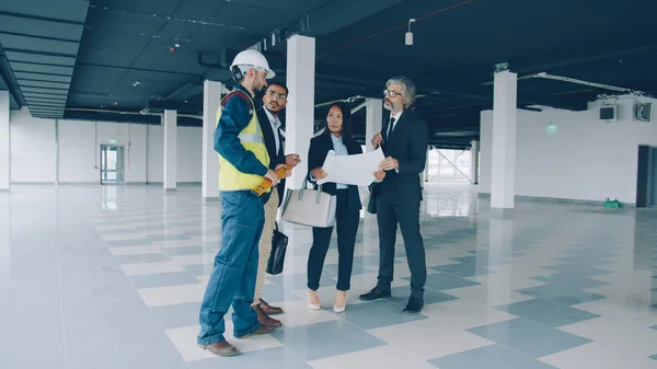 portrait of business team talking about maintenance of industrial building with glass walls and spacious halls. People and talks concept.