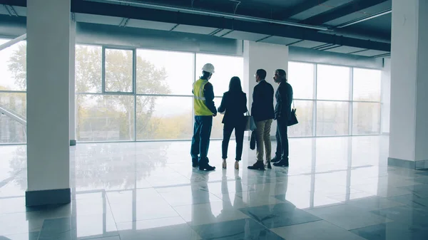 Diverse group of businesspeople standing inside newly constructed industrial building talking discussing real estate. People and business concept.