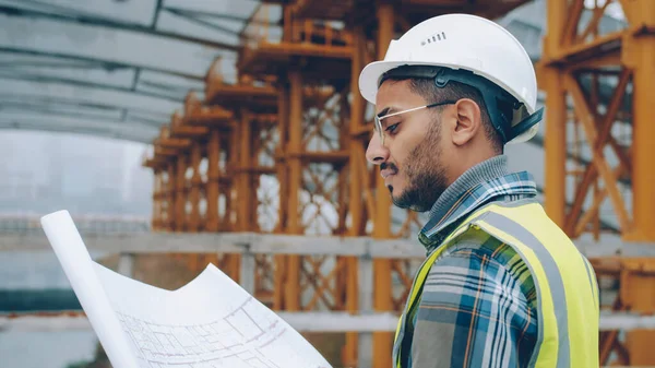 Portrait of engineer planning work at construction site looking at blueprint outdoors in industrial zone. People and occupation concept.