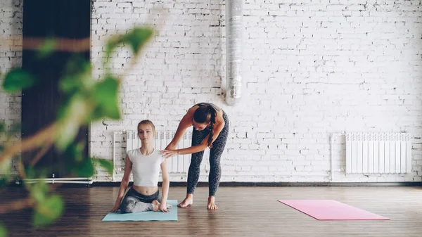 年轻苗条的金发女郎正在学习在现代瑜伽工作室的个人训练中 从友好的经验丰富的教练一条腿的国王鸽子的姿势 瑜伽大师理念的个体实践 — 图库照片