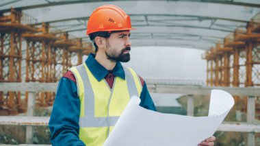 Üniformalı ciddi bir ustabaşının portresi planlara bakıyor ve şehir merkezindeki inşaat alanlarına bakıyor. Halk ve meslek kavramı.