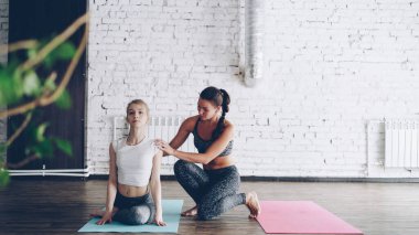 Neşeli çekici yoga öğretmeni yeni öğrenci ana inek yüzü modern spor merkezi bire bir sınıf sırasında poz yardım ediyor. Kadın gülümsüyor ve gülüyor, dostane bir atmosferde.