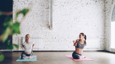 Genç sarışın kız Işık Studio kolay kadın eğitmen ile bireysel yoga pratik keyif alıyor. Kadınlar sıra parlak paspaslar üzerinde asanas yapıyoruz. Rahatlatıcı atmosfer.