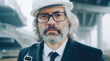 İnşaat alanında resmi giysiler ve miğfer giyen bina yöneticisinin yakın plan portresi. Halk ve kariyer kavramı.