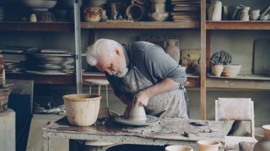 Üst düzey profesyonel potter genişletilmesi ve ıslak clayware yumuşatma potters çıkrık, kil kaseden yapıyor adam sakallı. Arka planda farklı el yapımı seramik figürler.