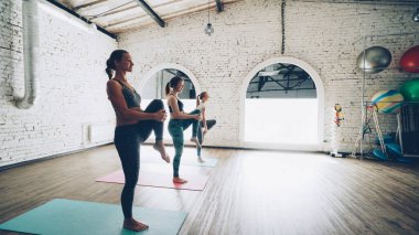 Dolly atış çok az genç kadınların hafif çatı stil spor salonunda karşı yoga egzersizleri yapıyor. Öğrencilerin pratik üzerinde yoğunlaşmıştır. Spor malzemeleri, fitness toplar ve paspaslar görülebilir.