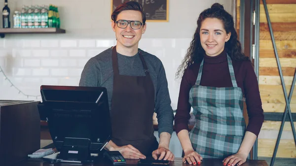 モダンなコーヒーハウスのレジの机に立って笑顔2人の若い見栄えのウェイターの肖像画 成功したビジネス 幸せな人々とフードサービスの概念 — ストック写真