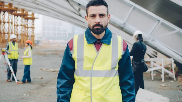 Portrait of construction employee wearing uniform standing outdoors in workplace with arms crossed and looking at camera. Career and people concept.