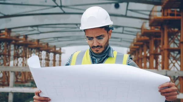 深刻なアラブ人の男のエンジニアは 建設計画をチェックし 工業地帯で屋外を見ています 専門家や職場のコンセプトを構築する — ストック写真