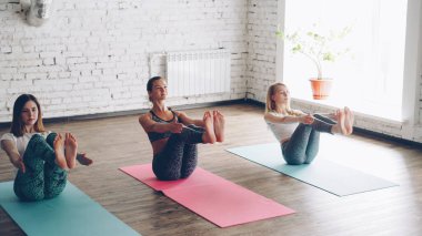 Pan çekim pratik yoga Dengeleme tekne poz ışık geniş odasında yapıyor ince genç bayanlar. Genç kadın counterpoising üzerinde duruldu, pratik tadını çıkarıyor.