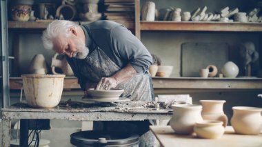 Deneyimli üst düzey yöneticisi küçük ev atölye bir çömlek tekerlek üzerinde düşük kil kase yapıyor. Seramik Banyo, el yapımı clayware ve potters araçları görülebilir.
