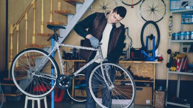 Genç deneyimli bakım elemanı dingillerdir tekerlek yerleştirerek ve onun işyerinde kulaklık ile müzik dinlerken tamir bisiklet montajı. Onarım ve insanlar kavramı.