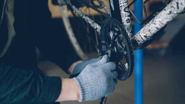 Close-up shot of strong male hands in protective gloves repairing broken bicycle treadle with wrench in workshop. Profession, people and maintenance concept.