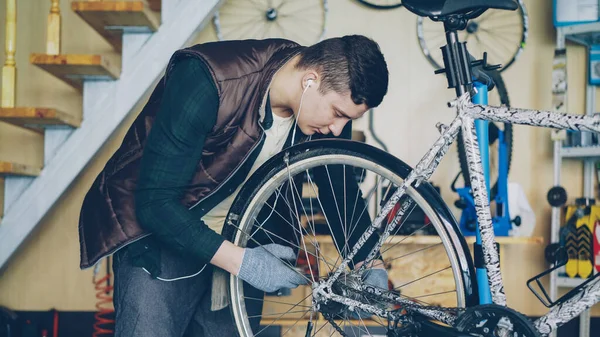 Experienced serviceman in gloves is assembling bicycle adjusting back wheel during servicing vehicle in workplace. Professional instruments, spare parts and equipment are visible.