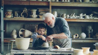 Bakım üst düzey dedesi genç sevimli torunu küçük atölye atma tekerlek üzerinde kil ile çalışmaya nasıl gösteriyor. Çanak çömlek, Aile hobi ve el sanatları kavramı.
