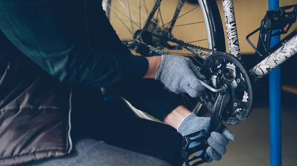 Close-up shot of strong male hands in protective gloves repairing broken bicycle treadle tightening loose joint with allen wrench in nice cozy workplace.