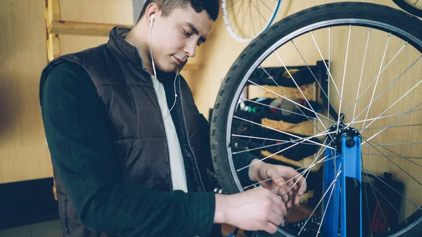 자전거를 서비스 이어폰으로 음악을 도구와 스포크를 자전거 바퀴를 집중된 정비공 — 스톡 사진