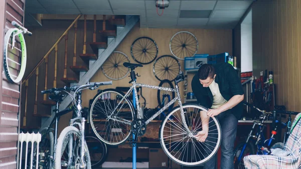 Experienced mechanic in casual clothes is busy checking handlebar and front wheel of bicycle then adjusting and fixing it with tools. Repairing cycles and people concept.