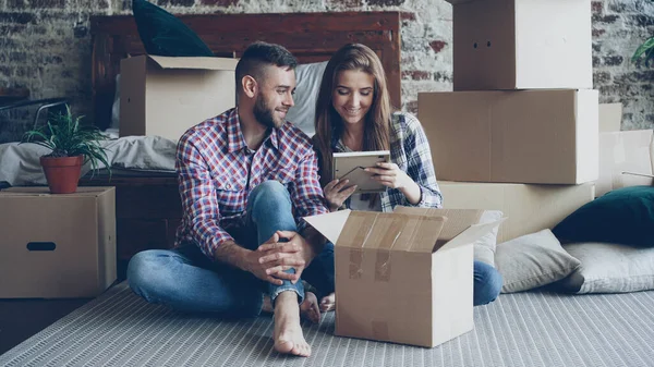 Happy couple is unpacking things after relocation opening carton box and looking at photos talking and laughing together. Moving to new house and relationship concept.