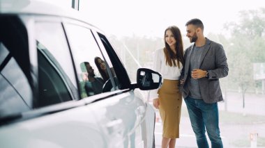 Çekici genç çift emin sakallı adam ve onun gülümseyen güzel kız arkadaşını yeni otomobil birlikte lüks araba araba satışı içinde bakarak ve konuşmayı tercih ediyor.