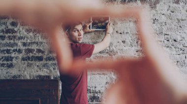 Neşeli genç adam karısına ile parmaklarını çerçeve şekli yapıyor ve ona bakarak, eller erkek ön planda iken tuğla duvar modern resim için yer seçimi.