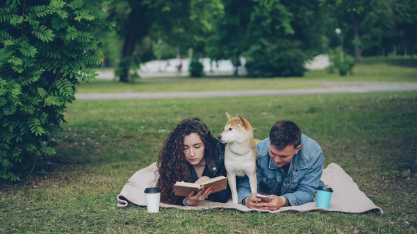 Молодая Семья Проводит Выходные Парке Женщина Читает Книгу Мужчина Использует — стоковое фото