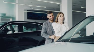 Çekici genç kadın sevgi dolu sevgilisinden yeni araba almayı, gözleri yaklaşıyor ve ona içinde motor Bayilik otomatik olarak önde gelen, onlar sarılma öpüşme ve.