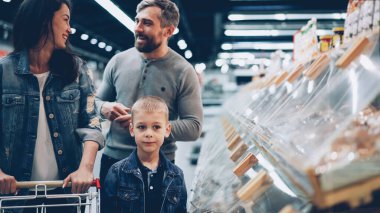 Mutlu aile anne, baba ve tatlı çocuk büyük bir süpermarkette yemek seçiyorlar. Konuşuyorlar, gülüyorlar ve gülüyorlar. İnsanlar ve alışveriş konsepti.