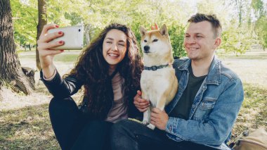 Gurur köpek sahipleri mutlu çift selfie ile eğleniyor ve smartphone vasıl seyir Füssing güzel evde beslenen hayvan alıyor. Modern yaşam tarzı, hayvanlar ve modern teknoloji kavramı.