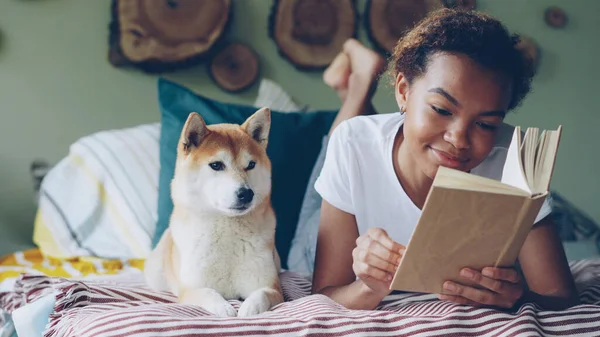 Jovem Afro Americana Está Lendo Livro Interessante Acariciando Seu Cão — Fotografia de Stock