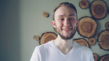 Yakın çekim portre yakışıklı genç adam kameraya bakarak ve gülümseyen beyaz T-shirt giyen sakallı. Çekici insanlar, iç ve mutluluk kavramı.