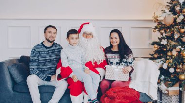 Mutlu aile anne, baba, çocuk ve Noel Baba 'nın portresi evdeki kanepede oturan kameraya bakıyor. Tatil ve kutlama konsepti.