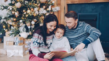 Aile annesi, baba ve oğul kitap okuyor ve Noel arifesinde evde konuşuyorlar, insanlar birlikte boş vakitlerin tadını çıkarıyorlar. Tatiller ve yaşam tarzı konsepti.