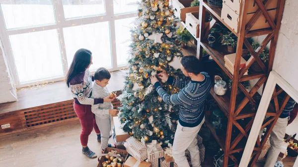 明るいボールをぶら下げて自宅でクリスマスツリーを飾る母親 父と息子の高い角度のビューとお祝いの活動を楽しんで話しています 人々と機会の概念 — ストック写真