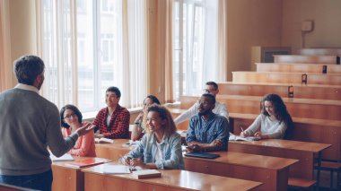Öğrenciler gülüyor ve onların önünde, konuşma ve el hareketi duruyor dostu Profesör için konuşmaya üniversite gençler. Eğitim, modern yaşam tarzı ve gençlik kavramı.