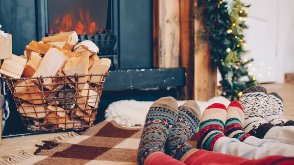 背景に暖炉のあるクリスマススタイルの靴下で大小の足のクローズアップ 家族は居心地の良い家で冬の休日を楽しんでいます — ストック写真