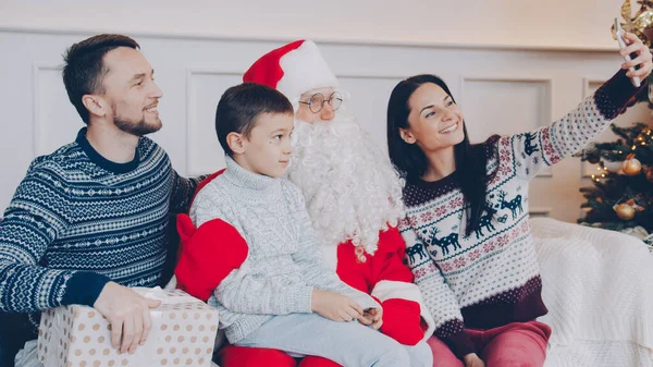 幸せな若い家族の母親 父と息子は自宅でスマートフォンのカメラを使用してサンタクロースと自撮り クリスマス 近代的な技術と人々の概念 — ストック写真