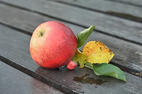 Czerwone jabłko z liści na drewnianym stole — Zdjęcie stockowe