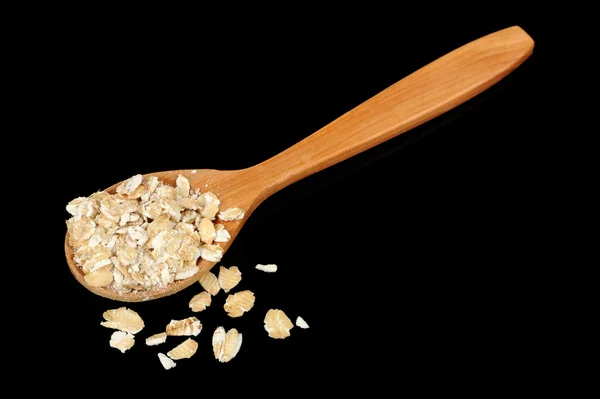 Cucchiaio di legno con fiocchi di avena su sfondo nero — Foto Stock